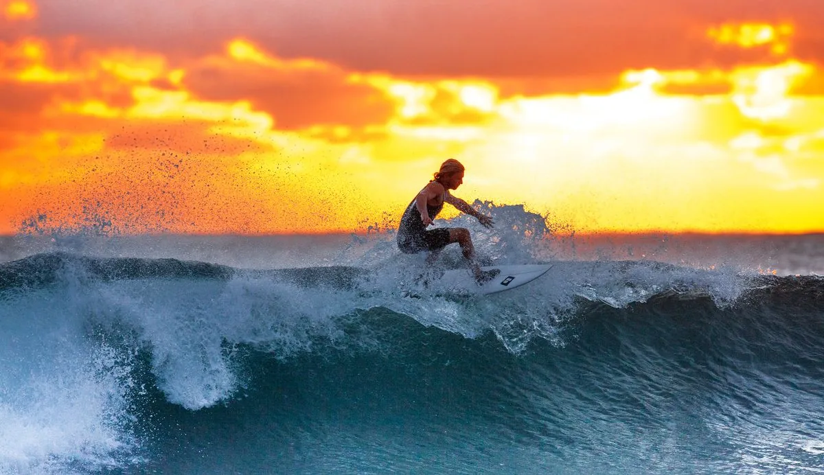 Silhouette of a surfer on a wave against an orange and purple sunset