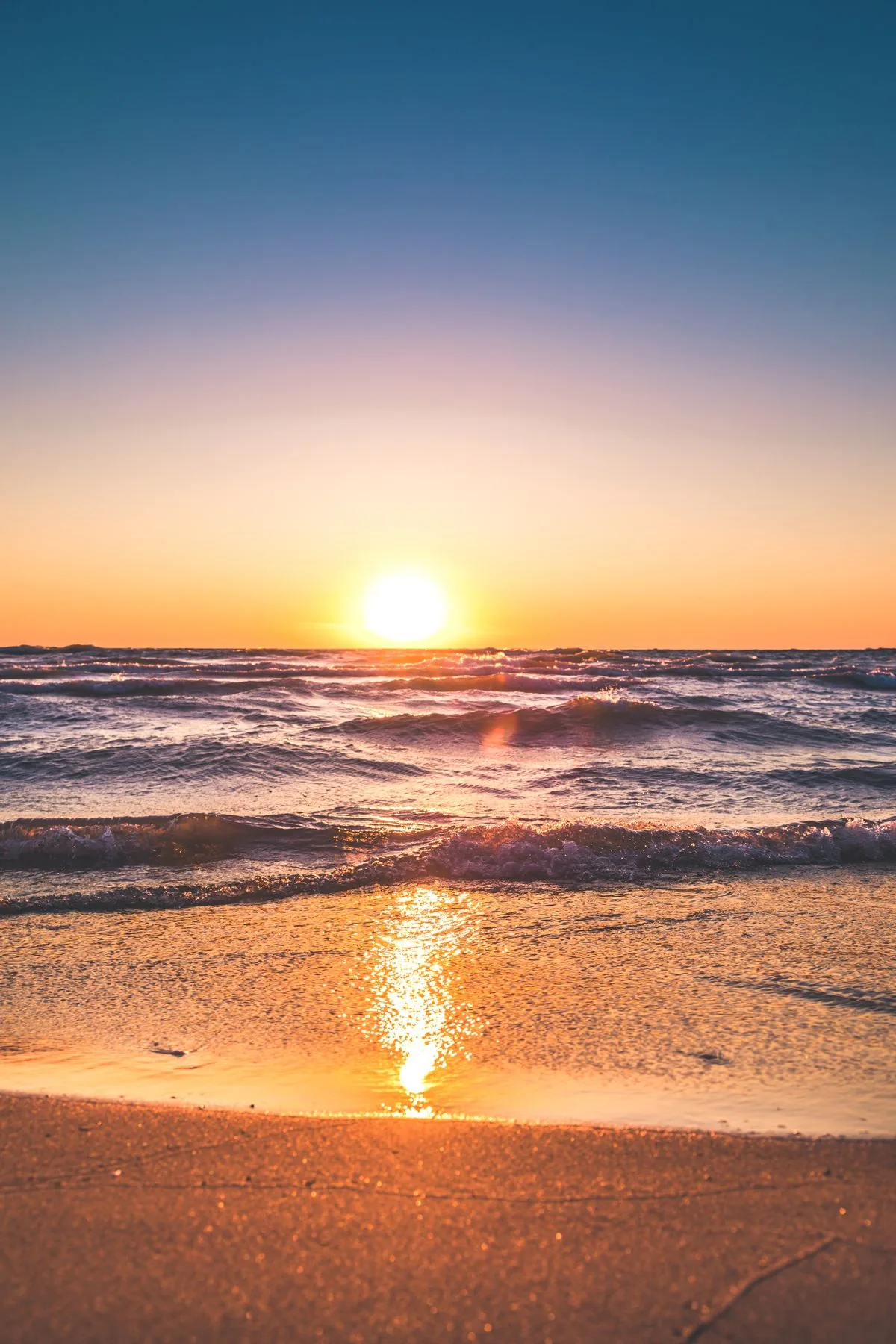 A surfer carrying a white board under an orange sunset
